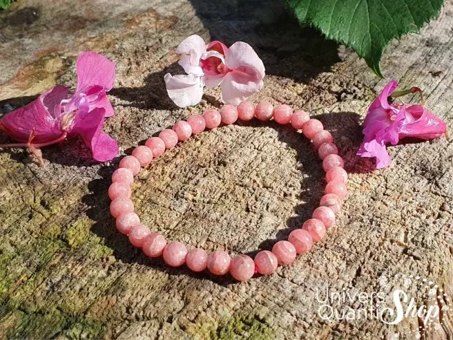 rhodochrosite signification bracelet 5mm posé sur un rocher avec des fleurs roses