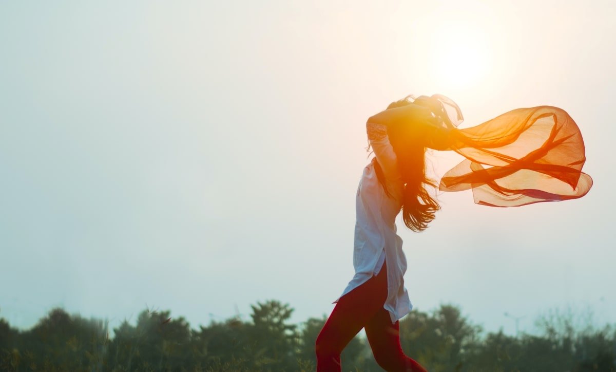 femme levant les bras dehors au soleil, force vitale grâce à son taux vibratoire