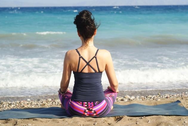 Femme de dos méditant sur la plage au calme