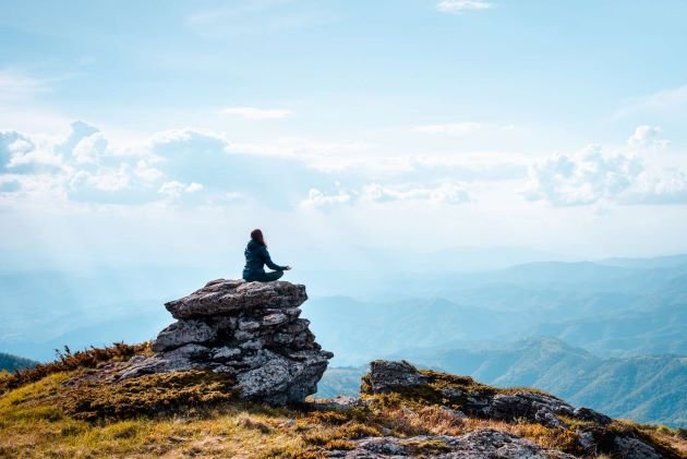 Femme méditant sur un rocher en haut d'une montagne