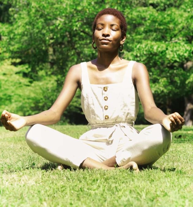 Femme méditant les yeux fermés dans l'herbe en plein soleil