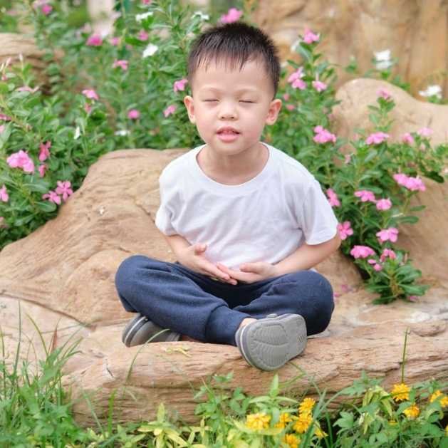 Pourquoi méditer ? Enfant heureux méditant dans un jardin fleuri.