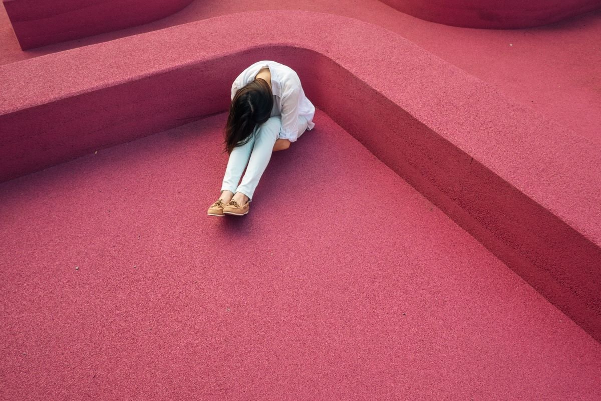 femme assise recroquevillée sur elle même sur une moquette rose rouge culpabilité