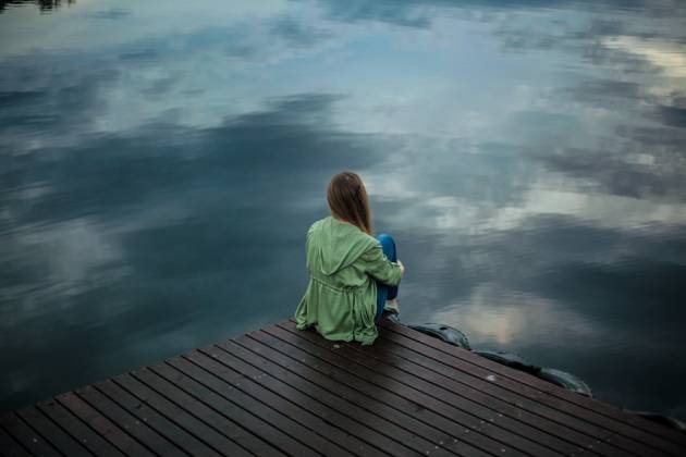 femme assise sur un ponton extérieur au bord d'un lac avec une veste verte hypersensibilité